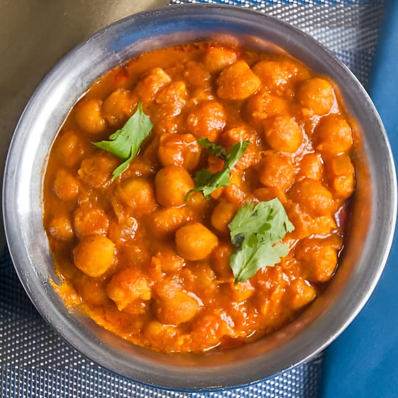A close-up of Indian chana masala, a chickpea curry, garnished with fresh cilantro in a metal bowl.