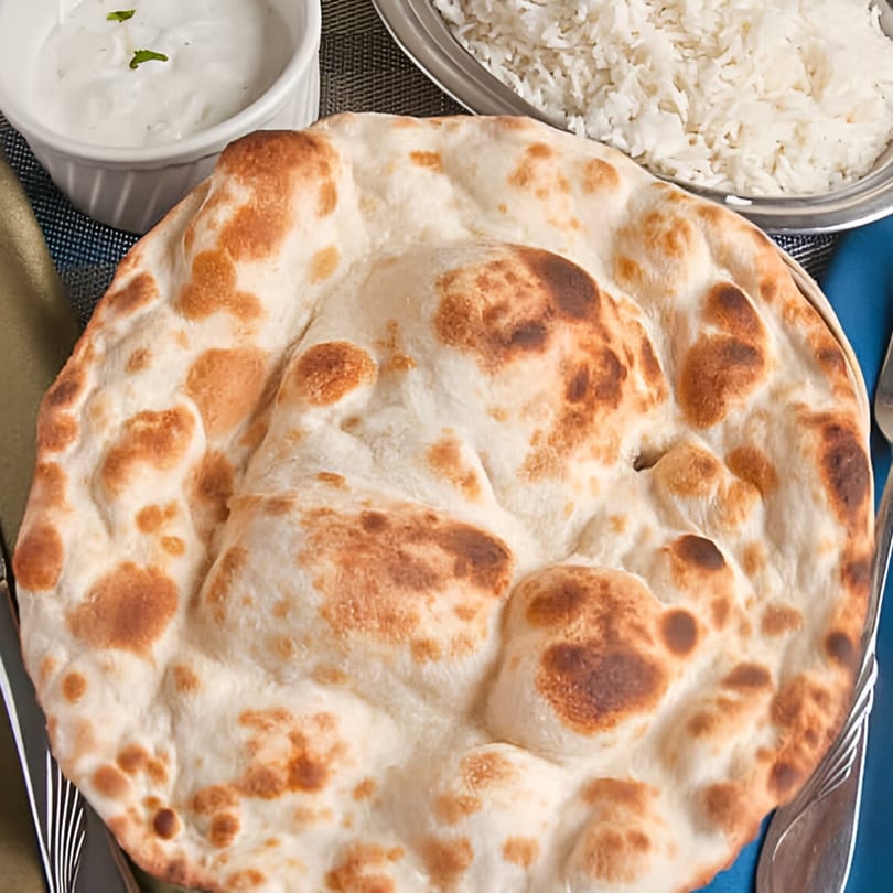 Indian naan bread with a side of white rice and raita, on a blue and green placemat.